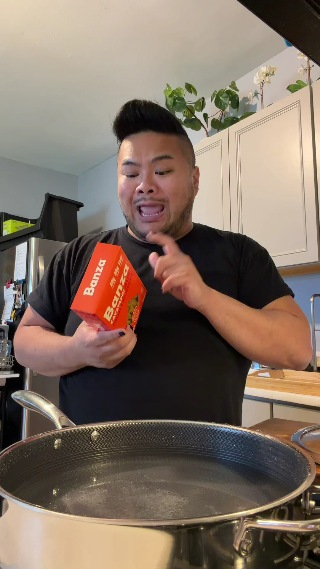 I hold a red Banza rotini box beside a pot while cooking the pasta in my kitchen.