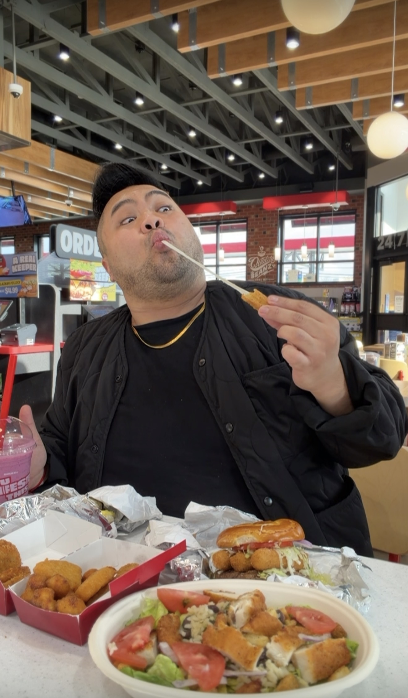 I stretch a strand of melted cheese from a sandwich while sitting behind a large spread of Sheetz food.