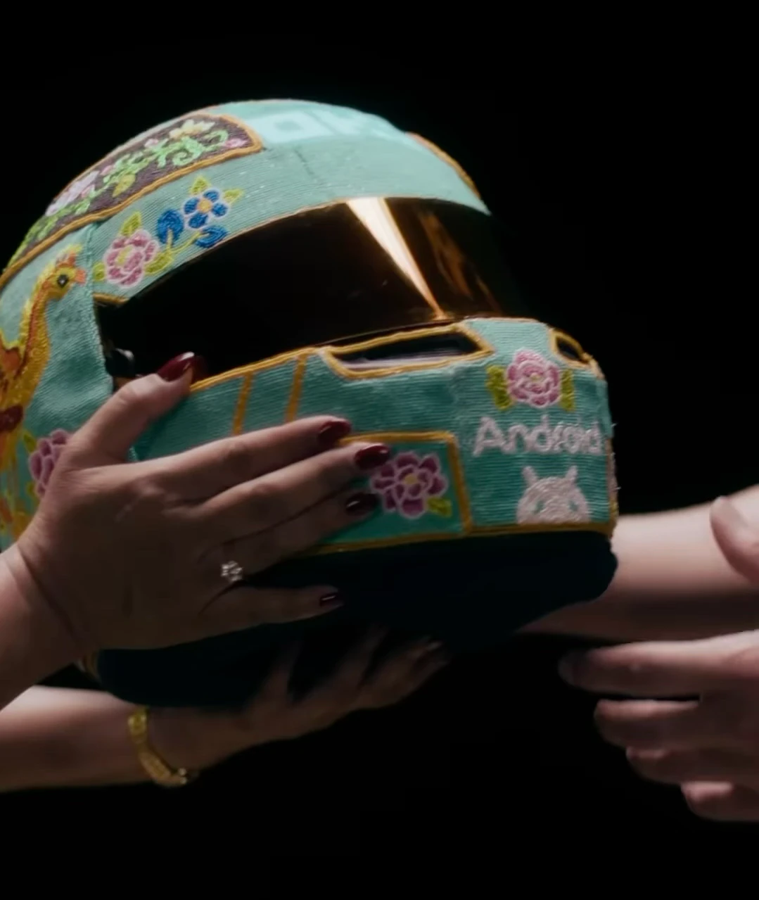 Hands pass Oscar Piastri’s turquoise beaded helmet against a black background.