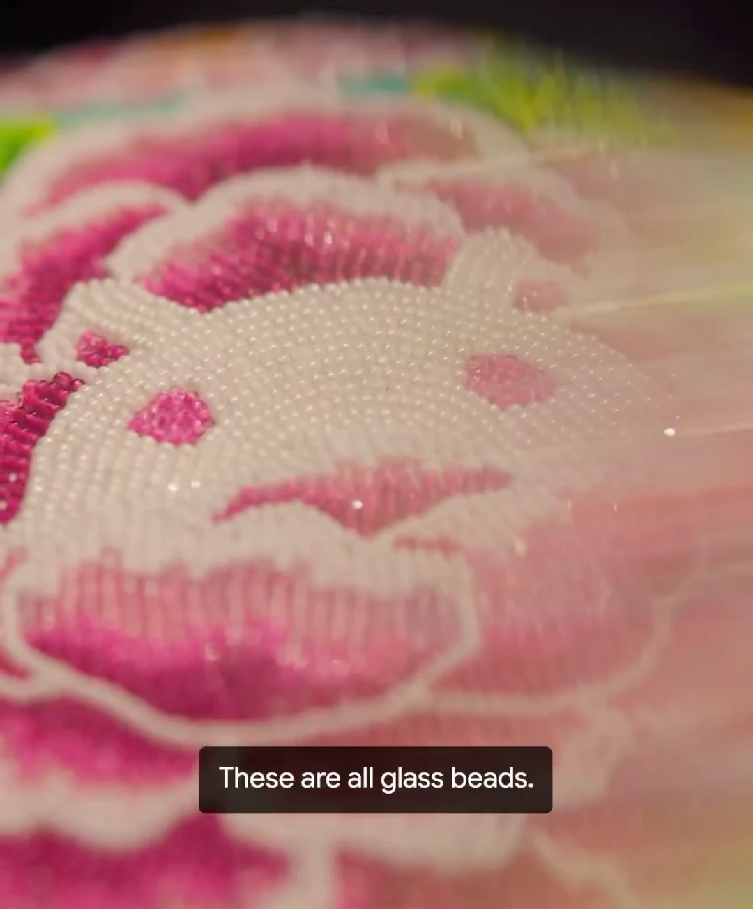 Rows of tiny pink and white beads form a floral pattern in a close-up view of Peranakan beadwork.