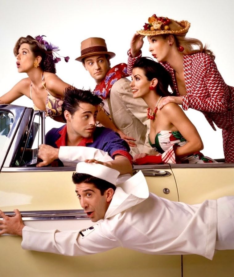 The cast of Friends crowds around a yellow convertible while Ross clings to its side.