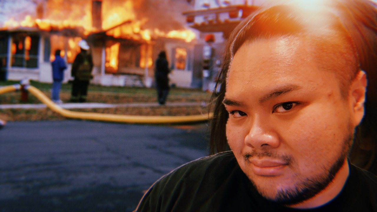 RV Mendoza looks toward the camera while firefighters respond to a burning house behind them.
