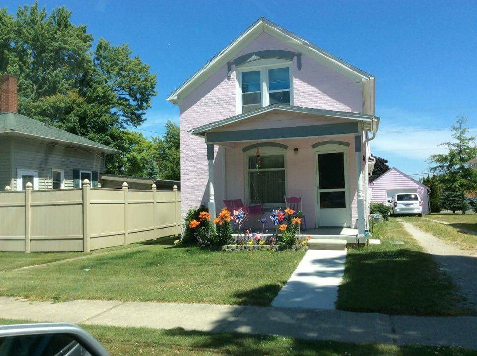 A pale pink two-story house with flowers along its front porch beneath a clear blue sky.