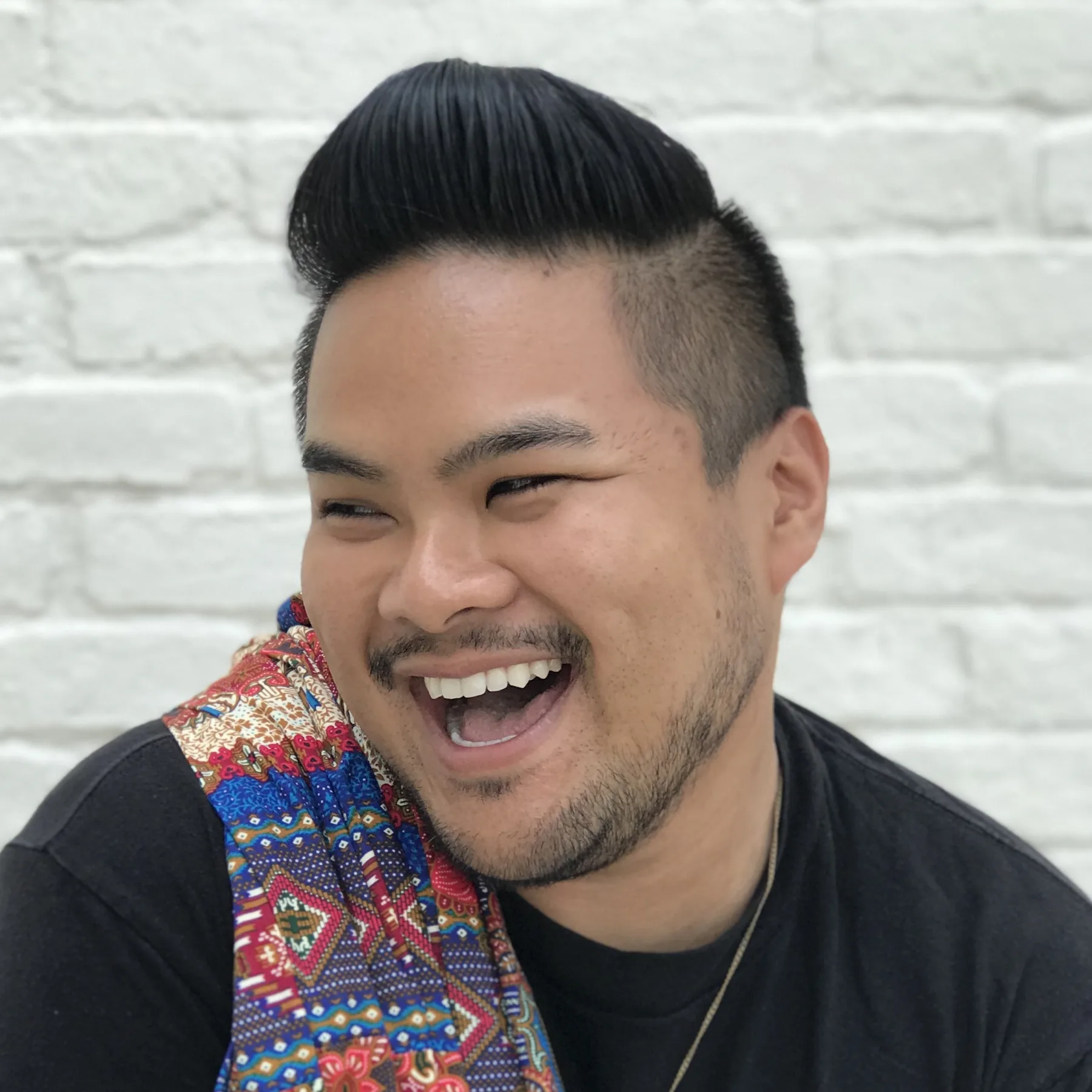 RV Mendoza smiling in front of a white brick wall.